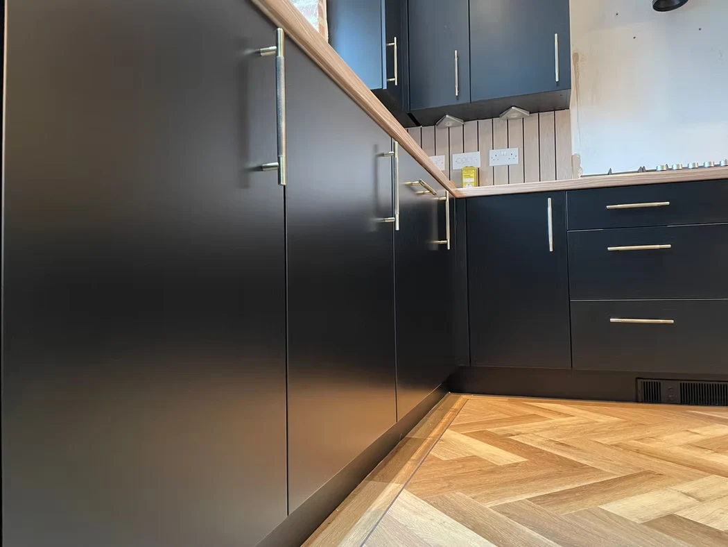 A close view of dark sprayed kitchen cabinets, handles and herringbone flooring